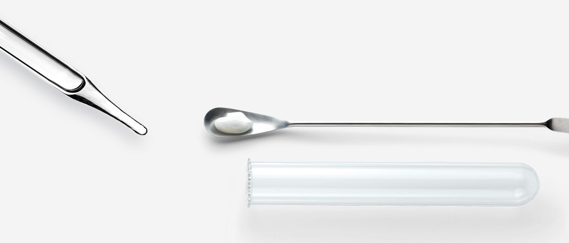 Laborspachtel mit weißer Substanz, Pipette und Reagenzglas
